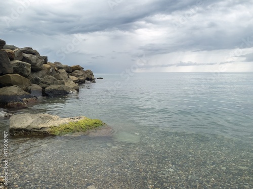 A thunderstorm front of rainy clouds over the calm waters of the Black Sea near a breakwater made of large boulders on a warm day in early autumn