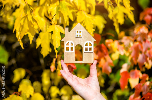The symbol of the house in the girl's hand on the background of yellow leaves
