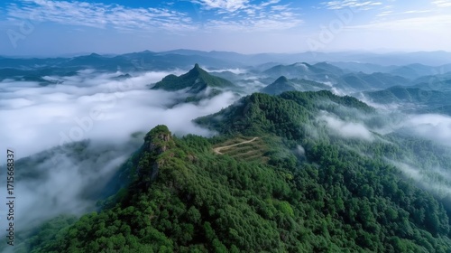 Aerial View of Lush Green Mountains Surrounded by Misty Clouds Under a Clear Blue Sky