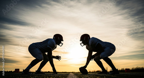 Silhouette of two American football players facing each other on scrimmage line, ready to charge, cloudy sky backdrop, competitive sports scene.