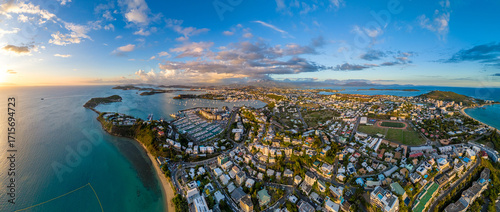 A stunning aerial panorama of Nouméa, the capital of New Caledonia, during a beautiful golden hour sunset. The city, marina, and turquoise bays are bathed in warm evening light
