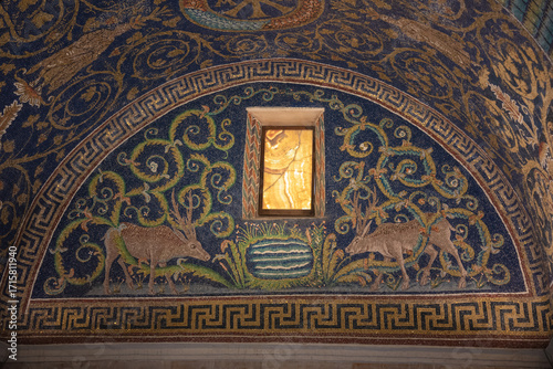 A detailed mosaic artwork depicts various decorative elements, including stylized plants, animals, and a small window, all crafted from small pieces of colored glass and stone