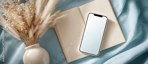 Phone on open book, beside feather grasses, on blue fabric