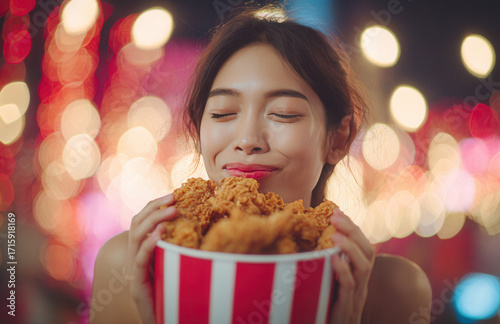 Woman enjoys a large bucket of fried chicken at a festive outdoor event during the evening