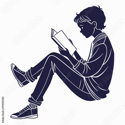 Silhouette of a young boy sitting cross legged on the floor engrossed in reading a book