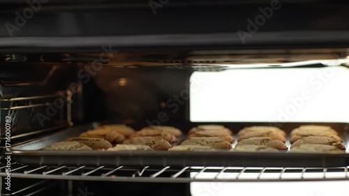 Freshly baked cookies on a tray inside an oven, with a warm glow illuminating the kitchen background