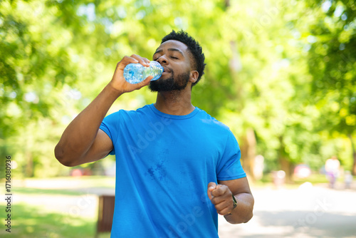 Billede på lærred Young man drinking water from a plastic bottle while taking a break during outdoor workout