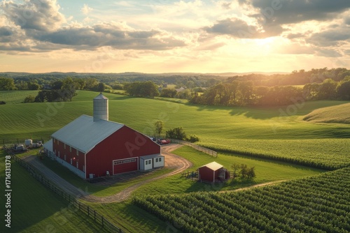 A scenic red barn and silo stand on a lush green farm with rolling hills under a golden sunset sky