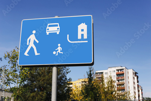 Blue road sign with pedestrian and children symbol. Residential zone traffic sign against clear sky. Safe street area with walking and playing zone. Urban transportation signal for public safety.