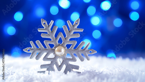 Silver Decorative Snowflake Ornament with Pearl Center on a Snowy Surface Against a Blue Bokeh Background for Winter and Christmas Themes