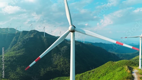 Aerial shot of a large wind turbine farm set on a beautiful green mountain range.