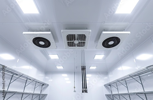 Low-angle view of a clean, white commercial cold storage room with three ceiling-mounted ventilation units and metal shelving along the walls, illuminated by bright recessed lights
