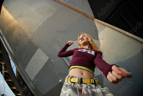 Caucasian girl dancing outdoors under urban structure, looking confident with expressive body language, wearing casual streetwear, representing Gen Z youth culture
