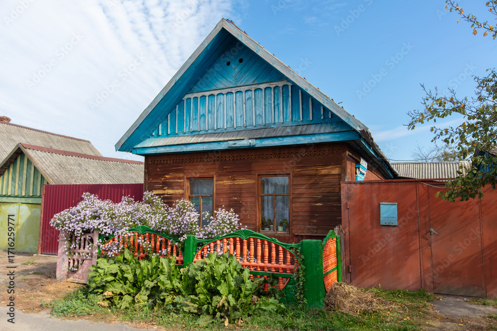 Fototapeta premium A narrow street in a village with small wooden houses and flower beds against a blue sky.
