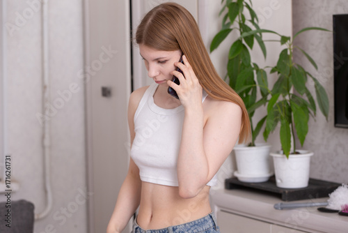 Young woman in casual outfit talking on phone while standing near plants in a modern indoor setting