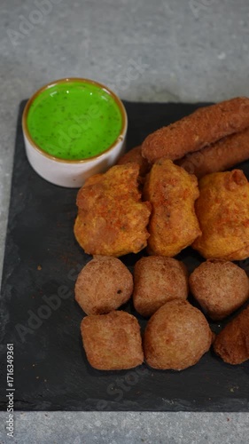 Assorted indian appetizers served on a black slate with green dipping sauce