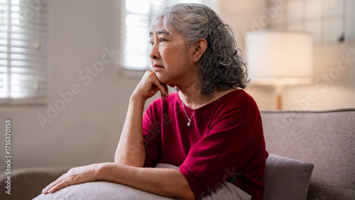 Foto Asian older woman sits on sofa thinking alone quiet home peaceful moment senior