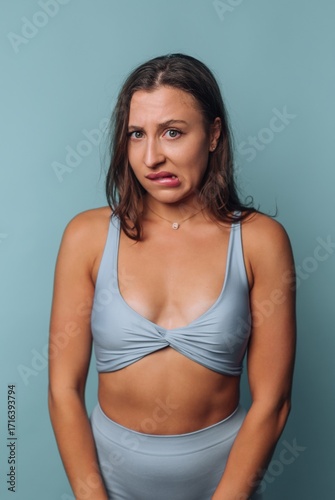 Model expresses discomfort in a light blue outfit against a solid backdrop in a studio setting