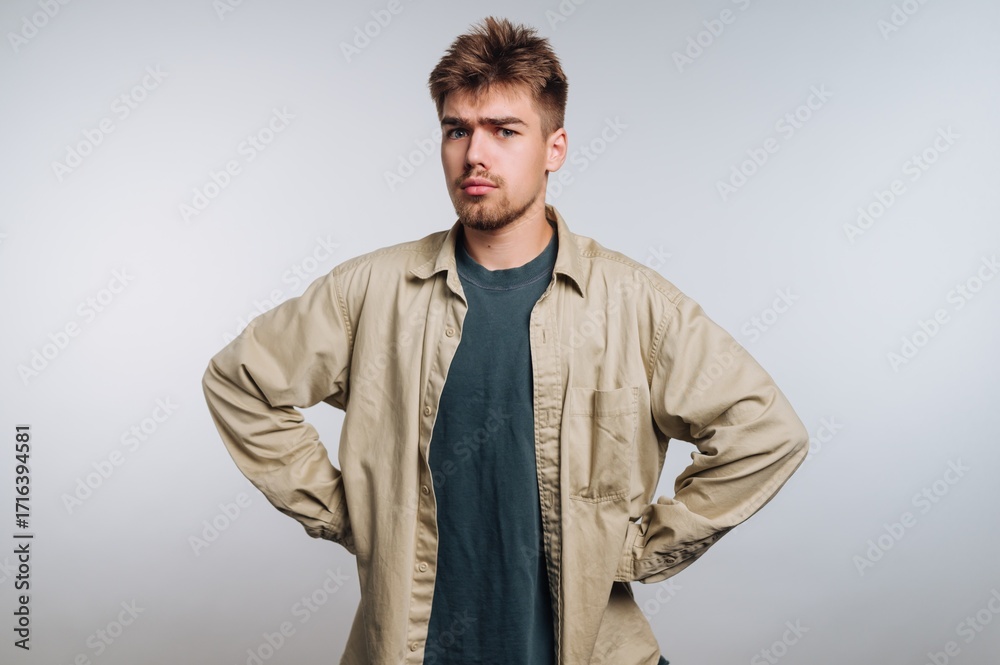 Fototapeta premium Young man poses with a serious expression against a plain background in a studio setting