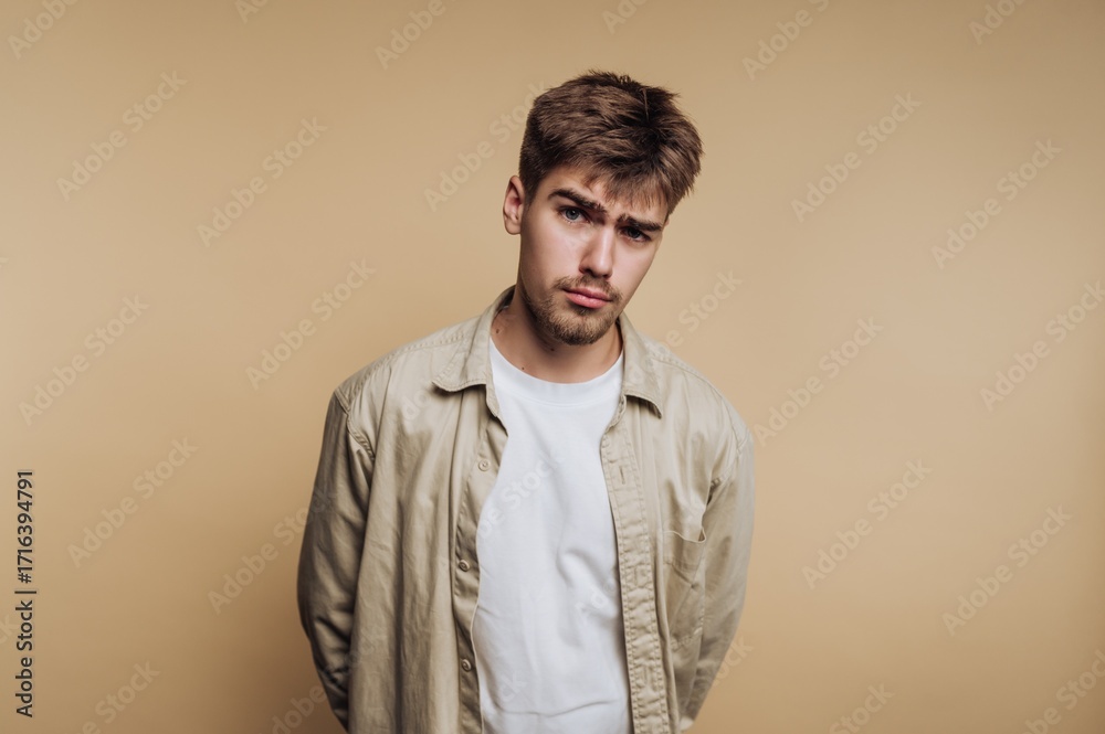 Fototapeta premium Young man poses with a serious expression against a plain background while dressed casually