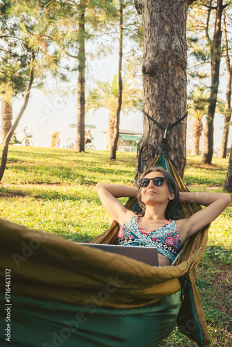 Happy Young brunette caucasian woman in hammock relax browse net work enjoy nap in park on black sea coastline on remote working holiday vacation in caucasus. Blogger travel influencer digital nomad