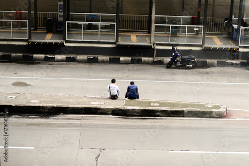 Obraz na plátně An authentic overhead view captures two men sitting casually on a concrete median in a dynamic urban street, reflecting moments of pause amidst the city's daily bustle and public transport