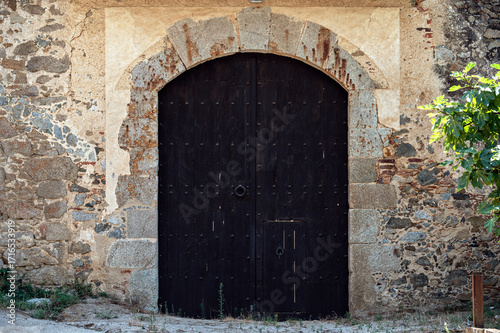 Large black arched gates with a wicket gate against the background of a stone wall for the entrance to an old building. From the World Doors series.