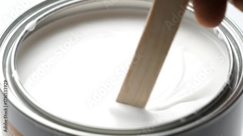 Mesmerizing close-up of thick white paint being slowly stirred in an open metal can with a wooden stick perfect for home renovation DIY projects creative arts a