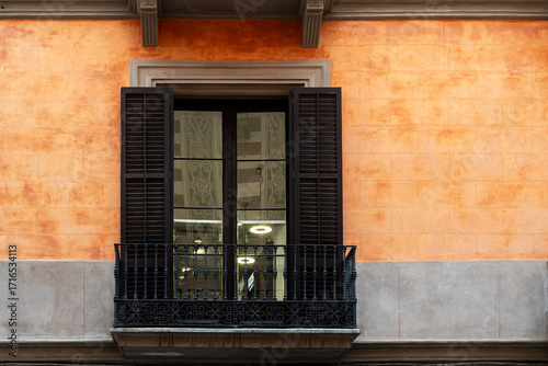 Rectangular window with balcony and dark brown shutters against wall of pink and gray tiles. From World Windows series.