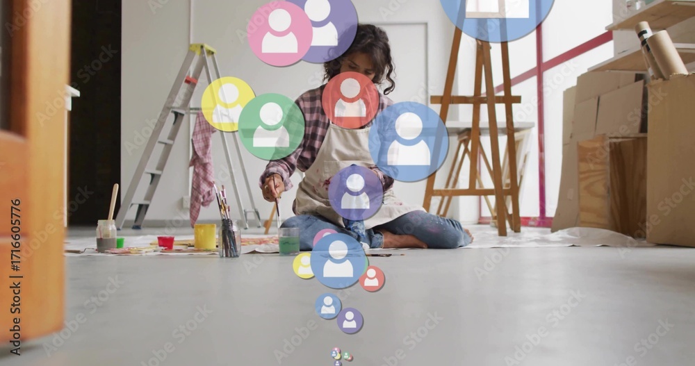 Naklejka premium Sitting adult artist painting on paper sheets in art studio, with art supplies and icon overlays