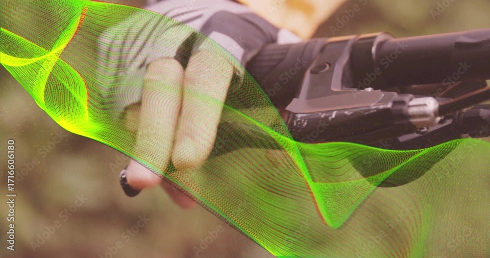 Fototapeta premium Gripping gloved hand in grey jersey on handlebar lever, forest trail green wave graphic, copy space