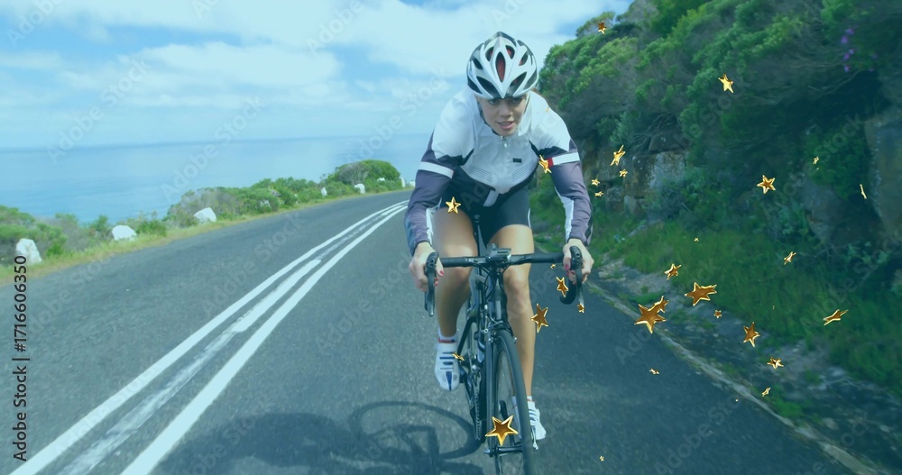 Obraz premium Riding cyclist on road bike wearing helmet along coastal road with golden star shaped sparkles