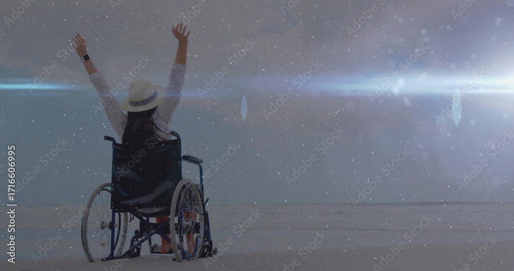 Fototapeta premium Person in wheelchair raising arms on sandy beach facing sea, with straw hat and wristwatch