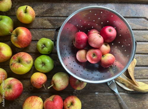 Close up of ripe red and green apples in a colander on a wooden table background the eating and cooking fruit freshly harvest organic allotment orchard garden in Summer interior flat lay view
