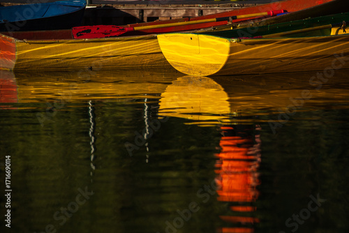 Old rowboats at the pier. Colorful colors. In the rays of the setting sun. Warm colors. Reflection in the water. Autumn days on the pond.