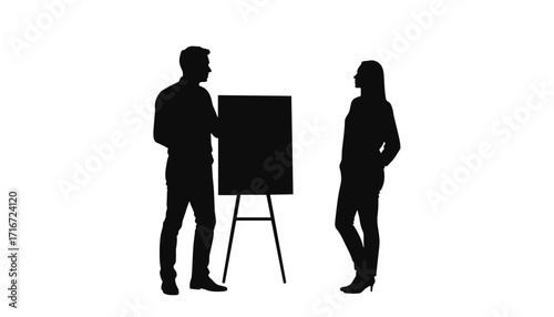 Silhouettes of man and woman discussing ideas in front of easel  