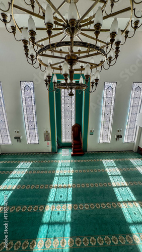 Beautiful interior view of a mosque with large decorative windows, traditional chandelier, and patterned carpet. Islamic architecture and religious atmosphere, suitable for concepts of faith, s