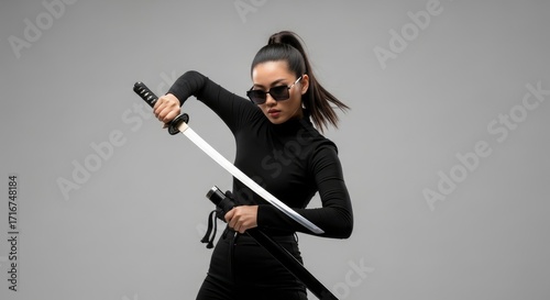 Woman in black wields a katana sword against a grey backdrop