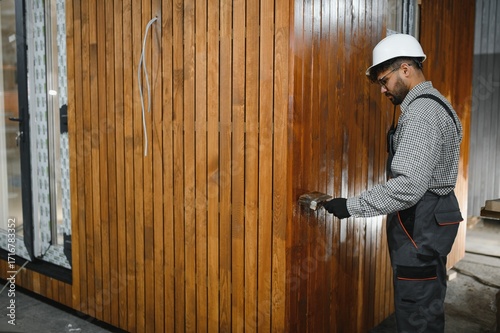 Construction worker applying varnish on wooden wall of modular house