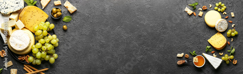 Obraz  z motywem Tray with different types of tasty cheese and grapes on dark background