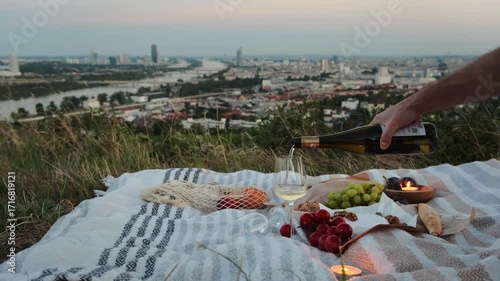 Cozy picnic on Vienna vineyards at sunset. Fruits, cheese, wine, and candles on the blanket, with evening city lights creating a warm, romantic, lifestyle and travel atmosphere.