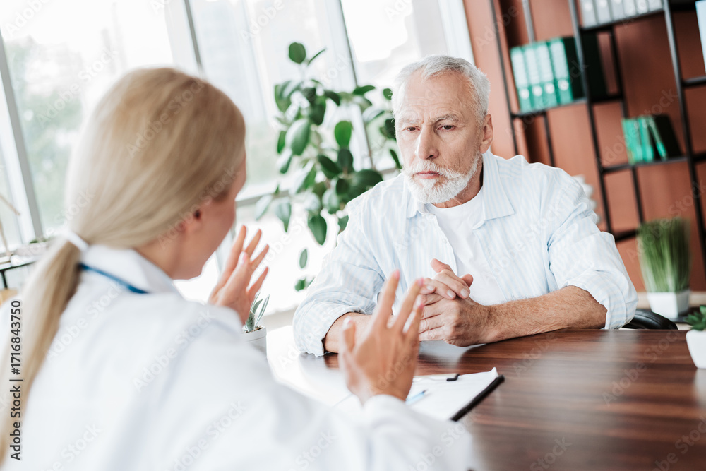 Obraz premium Doctor consulting an elderly patient in a modern clinic, addressing health concerns and providing medical advice
