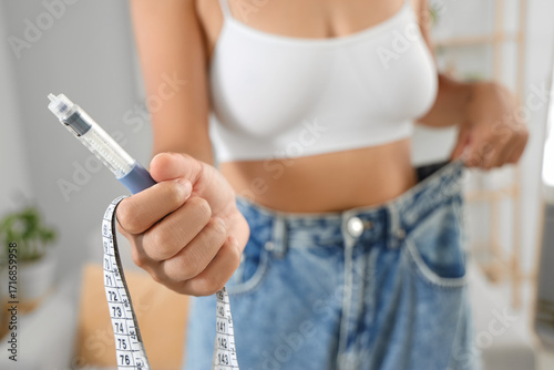 Fotografie Woman in loose jeans with injection and tape measure at home, closeup