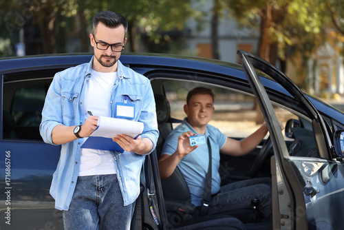Fotografi Male instructor with examiner after passing driving license test outdoors