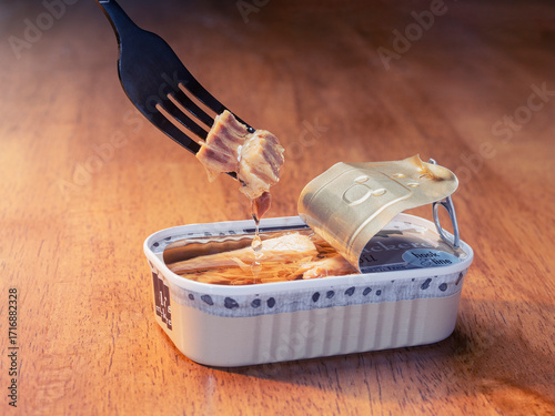 An open can of canned mackerel in oil with a fork pulling fish out of the can