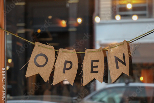rustic burlap open sign with individual letters strung together in shop window with reflection of street 