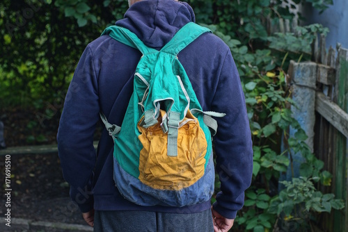 One old color backpack duffel bag hangs on the shoulder of a man in blue clothes on a spring street