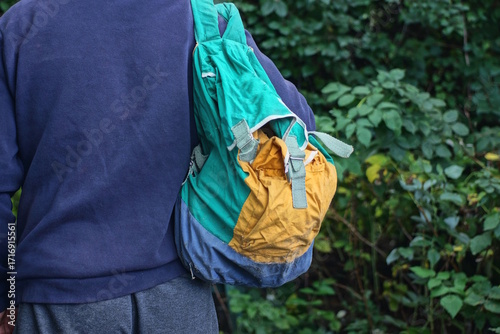 One old color backpack duffel bag hangs on the shoulder of a man in blue clothes on a spring street