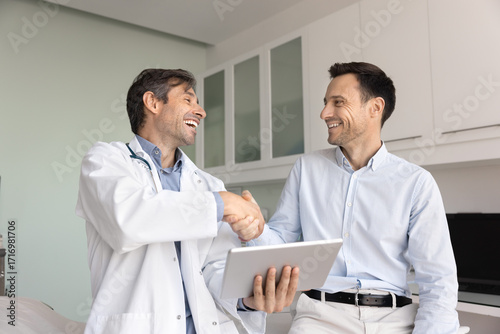 Foto Friendly doctor holding tablet shaking hands with male pharma representative
