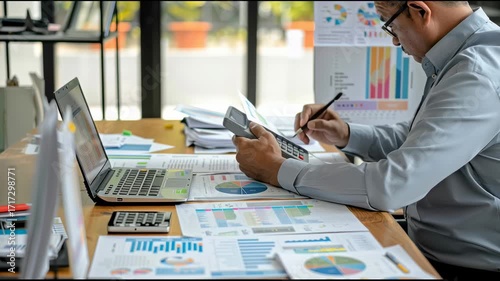 Detail-oriented accountant auditing financial statements and graphs on a reflective desk, combining manual calculations and digital record-keeping in a daylight-lit office.